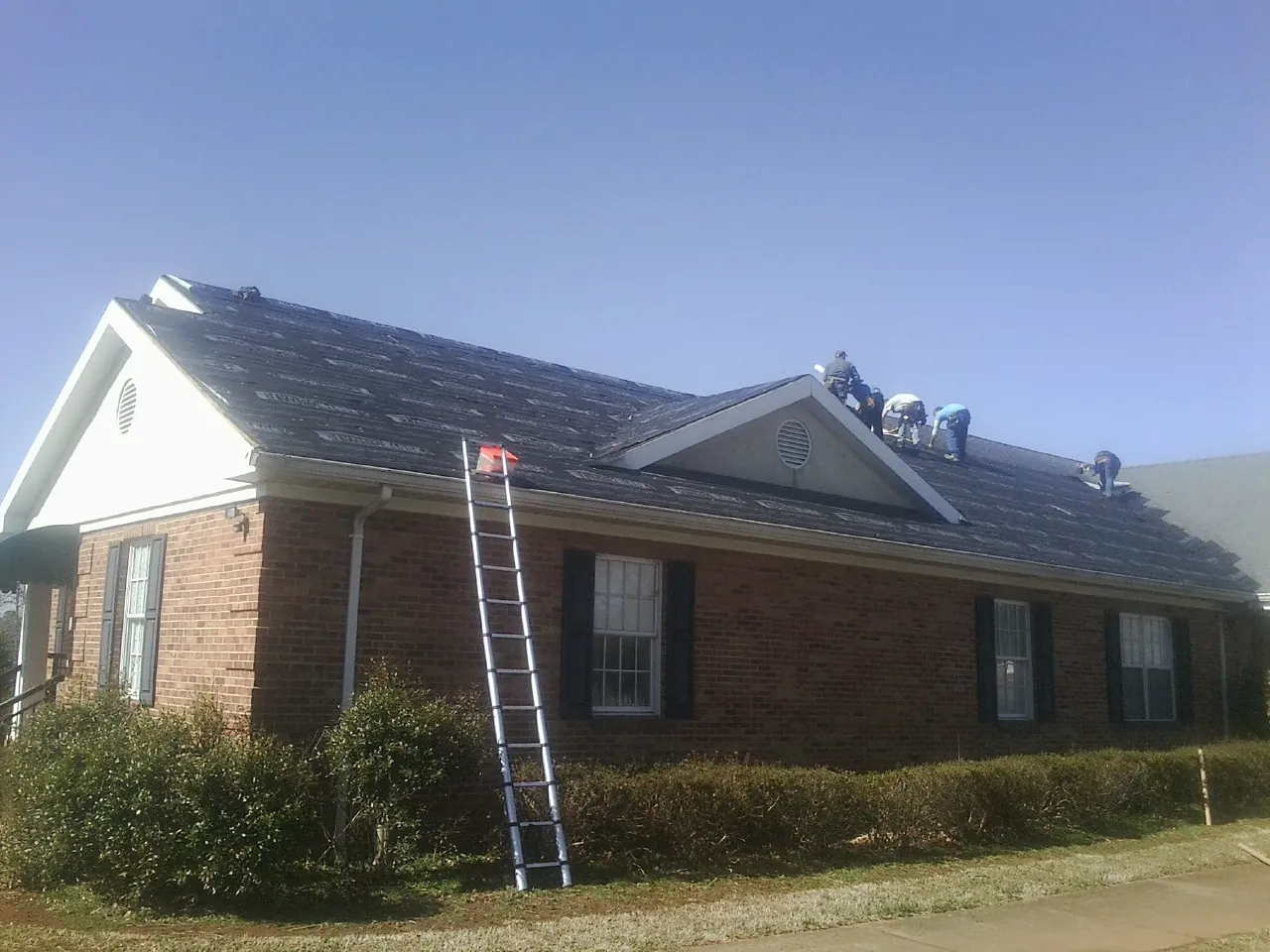 Crew tearing shingles off a brick ranch roof with a ladder set — Emergency Roof Repair work by our crew in Canfield