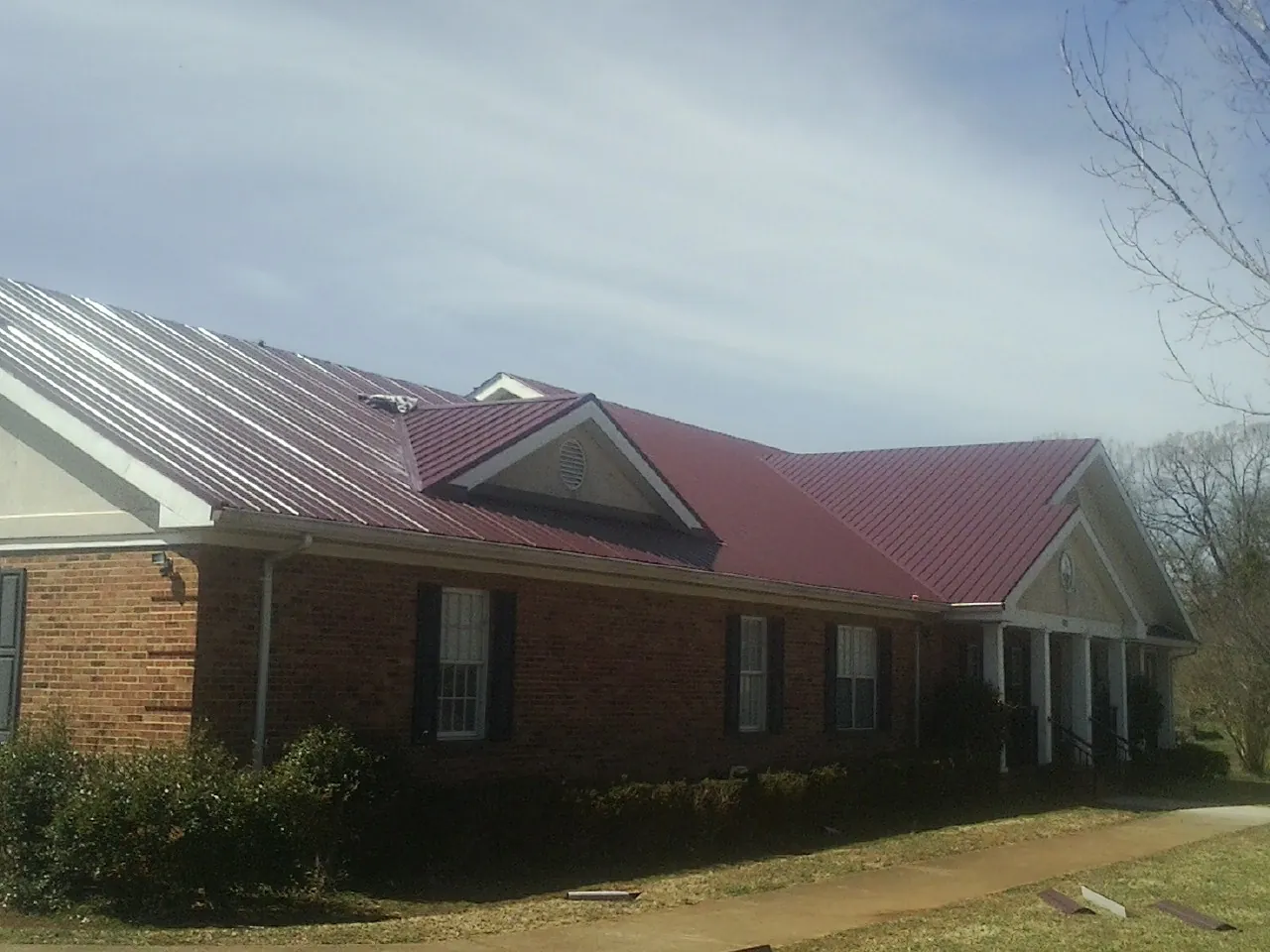 Red metal roof with gabled entries on a long brick building, from a Hail Damage Roof Repair job in Canfield
