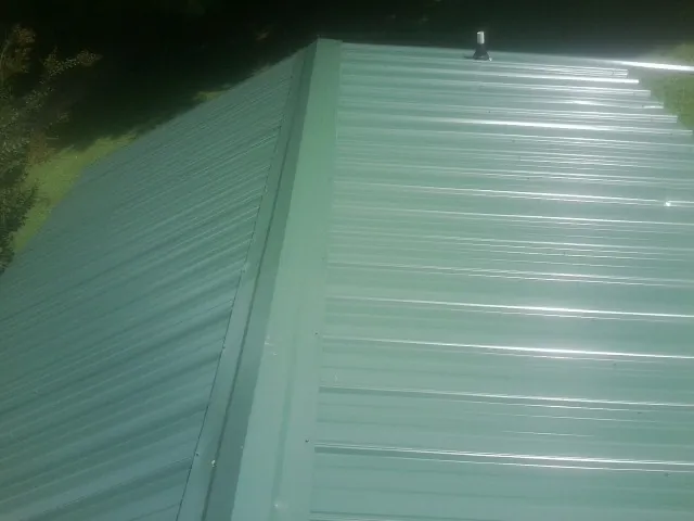 New green metal panels meeting at the ridge of a roof — Flat Roof Repair work by our crew in Canfield