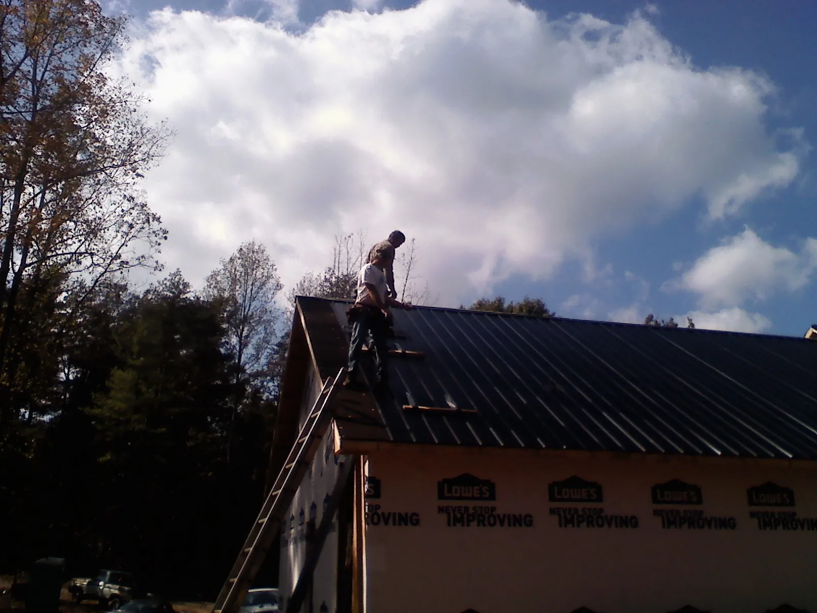 Roofer fastening dark metal panels high against a cloudy sky, from a Roof Inspection job in Canfield